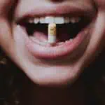 faceless woman with pill in teeth and nose piercing