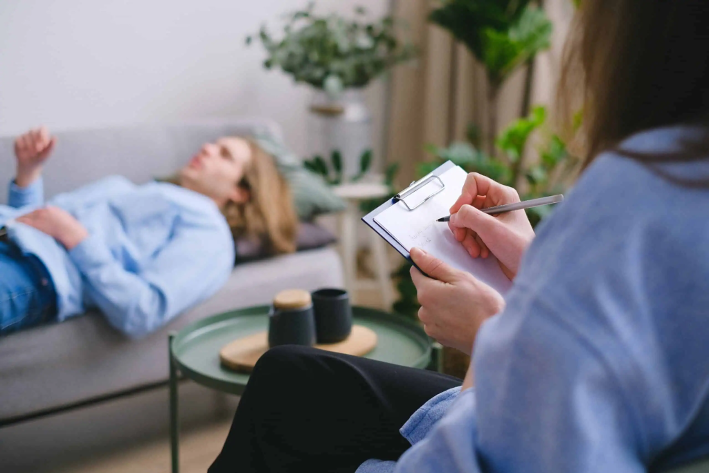 Therapist taking notes during a psychological counseling session with a young girl lying on a sofa, focusing on mental health, therapy, and psychological support services at Davenport Psychology.