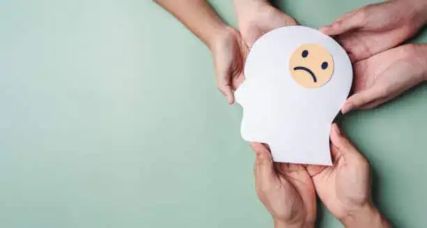 Sad face emoji on paper with a hand holding it, symbolizing mental health or emotional well-being issues.