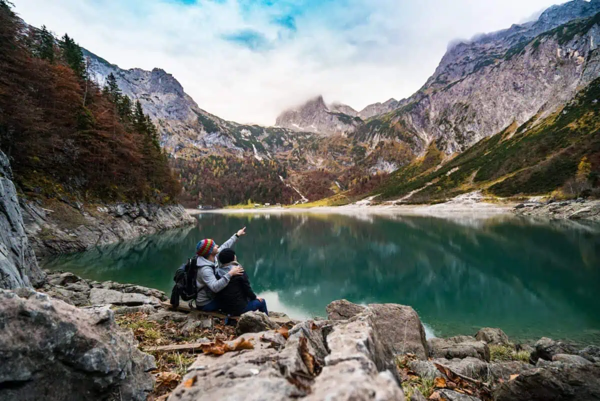 couple sitting on rock beside lake