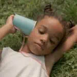 teenage girl laying on grass and holding blue paper cup at ear