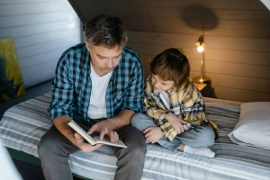 father and son sitting on bed while reading a book