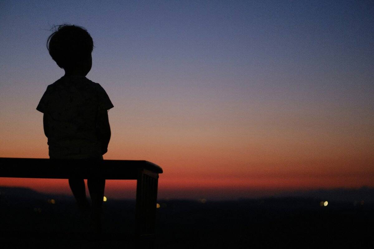 A young boy sitting alone on a bench, looking contemplative