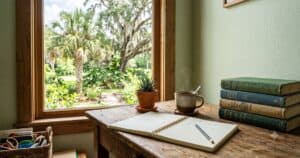 Bright homeschool corner with an open notebook, well-worn library books, and a Florida palm outside the window
